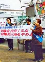 「核実験を再開するな」など書かれた横断幕を広げ持って立つ参加者たちと、そのとなりに立ってマイクを持ち訴える人。