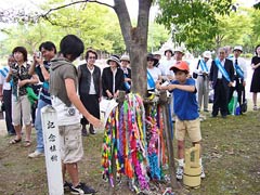 「東京の木」と、その周辺に集まった東友会代表ら。「東京の木」には千羽鶴にがいくつも掛けられており、子どもが新たに千羽鶴を掛けようとしている。