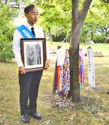 千羽鶴がいくつもかけられた「東京の木」と、隣に遺影を抱いて立つ濱住治郎さん。
