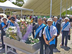 いくつもの花束が立ててある献花台と、周囲に立つ東友会と地域の代表たち。