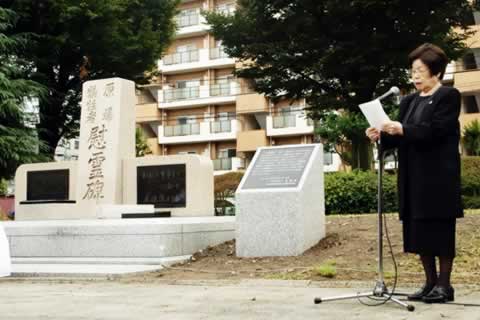 慰霊碑のそばに立ち、立てられたマイクを使って紙を読み上げる飯田マリ子代表理事。