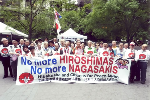 No more HIROSIMAS No more NAGASAKIS と書かれた横断幕を掲げ、折り鶴がデザインされたゼッケンをつけてならぶ代表団