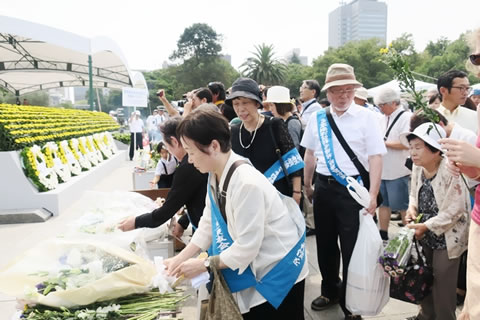 並べられた献花台の前には献花の列。たすきを掛けた東友会代表らが献花している。