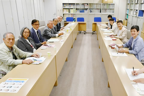 向かい合わせに並べられた机に着席する議員らと東友会の参加者たち。