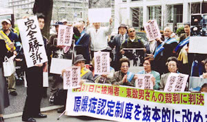 「完全勝訴」の文字を掲げる弁護士と、横断幕を前に「厚生労働省は控訴するな」と書かれた紙を持っている被爆者・支援者ら。