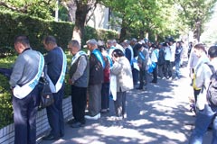 厚生労働省前の歩道に並んで立つ原告はじめ被爆者と支援者らが、厚労省のほうを向いて黙祷している。