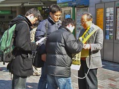 御茶ノ水駅頭、たすきを掛け署名板を持つ宣伝行動参加者と、その周りで署名したりチラシを読む青年ら。