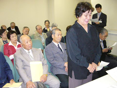 机の前に立って申請書を提出する雌性者。順番待ちの人は椅子に座っている。