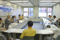 長方形に並べられた机に着席し議論する参加者たち。