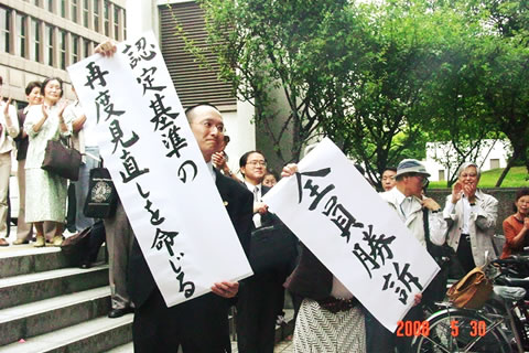 5月30日、大阪高裁前で「全員勝訴」「認定基準の再度見直しを命じる」の文字を掲げる弁護士たちと、拍手する支援者たち