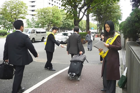 東京高裁前で、マイクを使い訴える弁護士と、通行人にチラシを手渡す行動参加者。