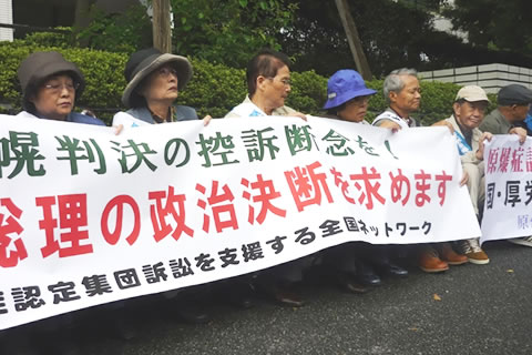 厚生労働省前歩道で、札幌地裁判決後に座り込みを行う被爆者・支援者。「札幌判決の控訴断念を！」「総理の政治決断を求めます」と書かれたものなど、横断幕を掲げている。
