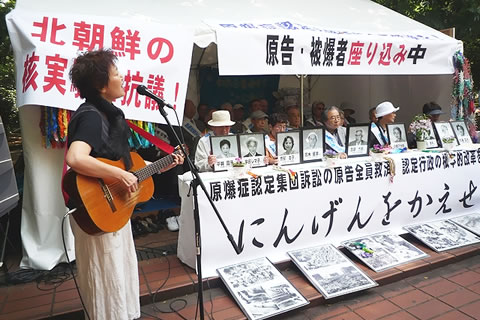 厚生労働省向かい、日比谷公園に座り込み行動のために建てたテントで、遺影を掲げて座る被爆者たち。ギターで弾き語りする横井久美子さんも。