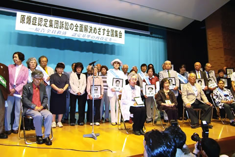 星陵会館での全国集会、舞台上に集まった人びとの写真。東京原告団も遺影を持って舞台に上がっている。