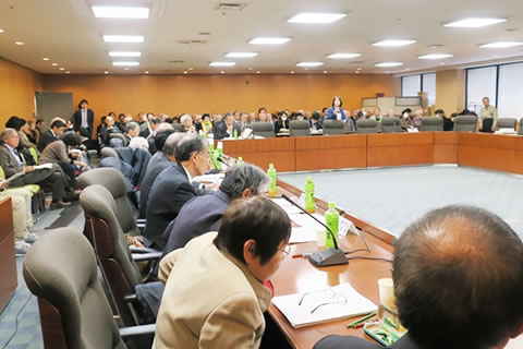 広い会議室、口の字型に並べられた机に着席する100人を超える参加者