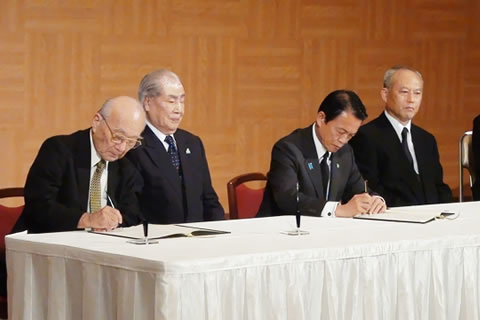 被団協代表2人と総理大臣、厚生労働大臣が一つのテーブルに横並びに座っている。被団協代表の1人と総理大臣がそれぞれ確認書に署名している場面。