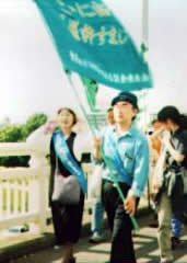 東友会の旗を持ち、たすきを掛けた被爆者が他の参加者とともに歩いている。