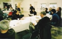 どのイベントの写真であるか不明。奥に発言をする人が立っており、並べられたテーブルで席についてそれを聴いている参加者たち。