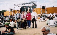 野外の大きいステージのあるひろばで。代表4人は立って写真の真ん中に。その他の参加者の人々は地べたに座っている。
