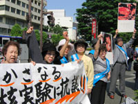 アメリカ大使館前にて「度重なる核実験に抗議!!」の横断幕を掲げて、こぶしを挙げる被爆者ら。
