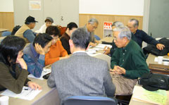 「つどい」会場で、机の席に座り見舞金を届ける相談をする参加者たち。