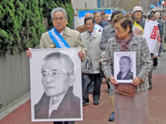 縦80センチほどに大きく引き延ばした東さんの写真を持つ東友会会長・藤平さんと、東さんの遺影を抱いた東朝子さんを先頭に法廷へ向かう被爆者・支援者たち。