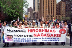 「NOMORE HIROSHIMAS NOMORE NAGASAKIS」と書かれた大きい横断幕を9人もの人が横に並んで先頭に掲げ、ニューヨークの車道をパレードしている。