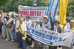 「原爆症認定集団訴訟の勝利を」など書かれた横断幕を掲げる、たすきを掛けた原告・支援者ら。厚生労働省に向かってこぶしを挙げている。