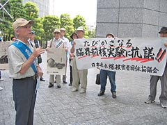 「たびかさなる臨界前核実験に抗議!!」と書かれた横断幕などを掲げて立つ被爆者たち。