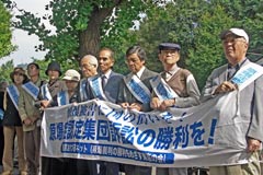 「原爆症認定集団訴訟の勝利を!」と書かれた横断幕を掲げ、歩道で厚生労働省に向かって立つ原告ら。