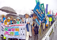 「国民平和大行進」など書かれた横断幕を持つ人を先頭に車道を歩く行進の列。東友会の旗のほか、さまざまな団体ののぼりや旗が続いている。