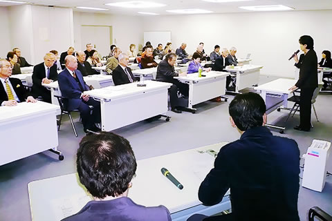 東京都職員と東友会の参加者が、向き合う形で並べられた机に着席している。一人が会場前方(都職員着席側)で立って、マイクを使い話をしている。