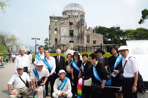 原爆ドームを背景に並ぶ代表団の集合写真。東友会のたすきを掛けている人が多い。