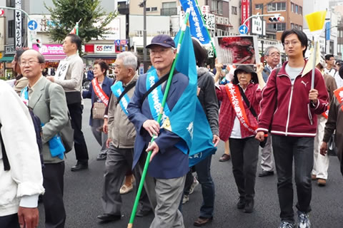 旗などを持ち、たすきを掛けて浅草を歩く参加者たち