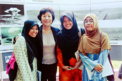 マレーシアでの原爆展会場にて、明るい色の衣装を着てほほえむ3人のイスラム系女学生と山田さんが並んでいる。