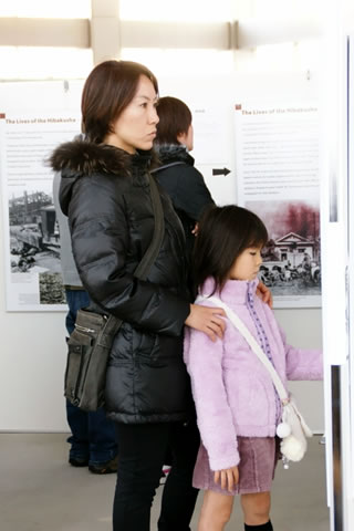 ついたてに展示されたパネルを見る親子。親の両手は子どもの肩に乗せられている。