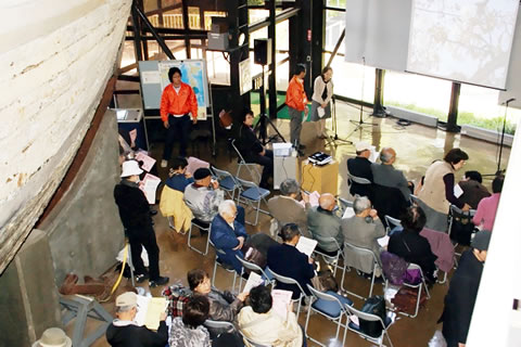 第五福竜丸展示館内、船体のわきに並べられた椅子に座る参加者たち。