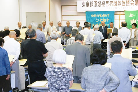 並べられた机のそれぞれの席で立って歌う参加者たち。