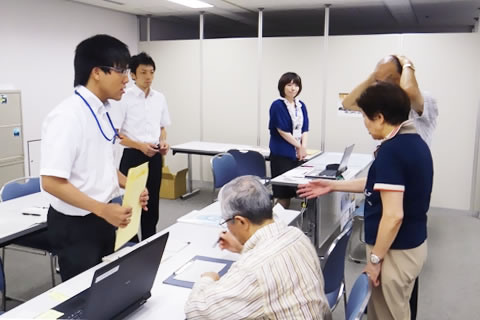 広島市の死没者名簿照合窓口にて、あいさつして名簿を渡す東友会代表と、受け取る広島市職員。