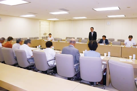 広い部屋、対面して並べられた机に着席する議員と東友会役員。