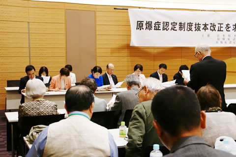 対面して並べられた机に着席する参加者たちが、メモを取るなどしている。