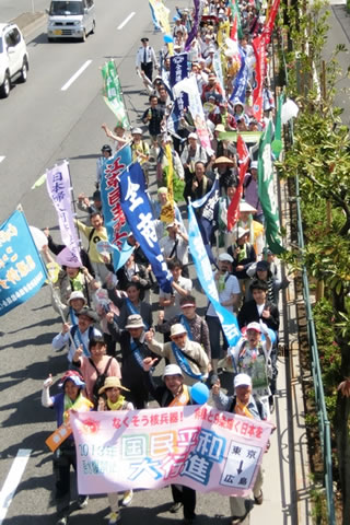 「国民平和大行進」と書かれた横断幕を持つ人たちを先頭に車道を進む行進。団体の名前などが書かれたのぼりや旗がいくつも掲げられた列が長く続いている。
