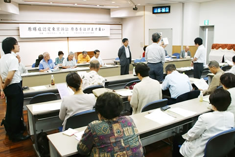広い部屋に並べられた机に着席する参加者。紹介された弁護士たちが、それぞれ座っていた席で立っている。