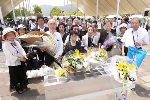 平和記念公園にしつらえられた献花台の前、花束を持って立つ東友会代表団の集合写真。