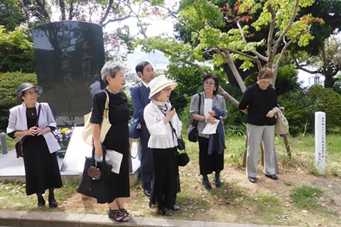 長崎市平和公園内、クロガネモチの木の前に立つ東友会代表たち。