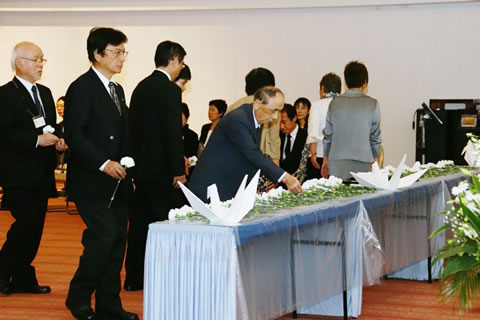 大きい折り鶴の飾られた献花台の前に並び、献花していく参列者たち。