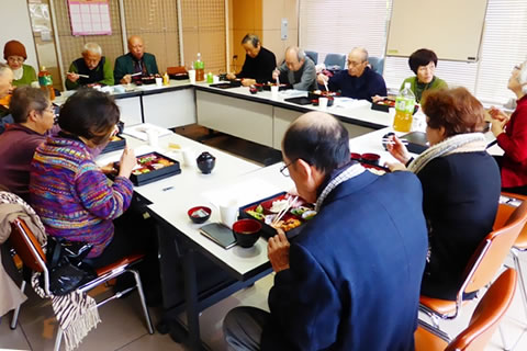 長方形に並べられた机に着席し、談笑しながら食事する参加者。