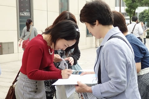 有楽町マリオン前での署名行動で、笑顔で会話しながら署名に応じる人。