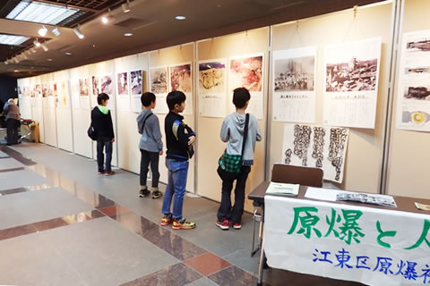 20メートルほど横に連ねて並べられた、高さ2メートルほどのついたてに「原爆と人間展」パネルが展示されている。手前の机に「原爆と人間展」の文字。