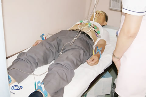 ベッドに寝て、心電図の装置を手首・足首・腹部に着けている男性